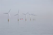 Windturbines op een grijze dag met rood schip op de achtergrond.
